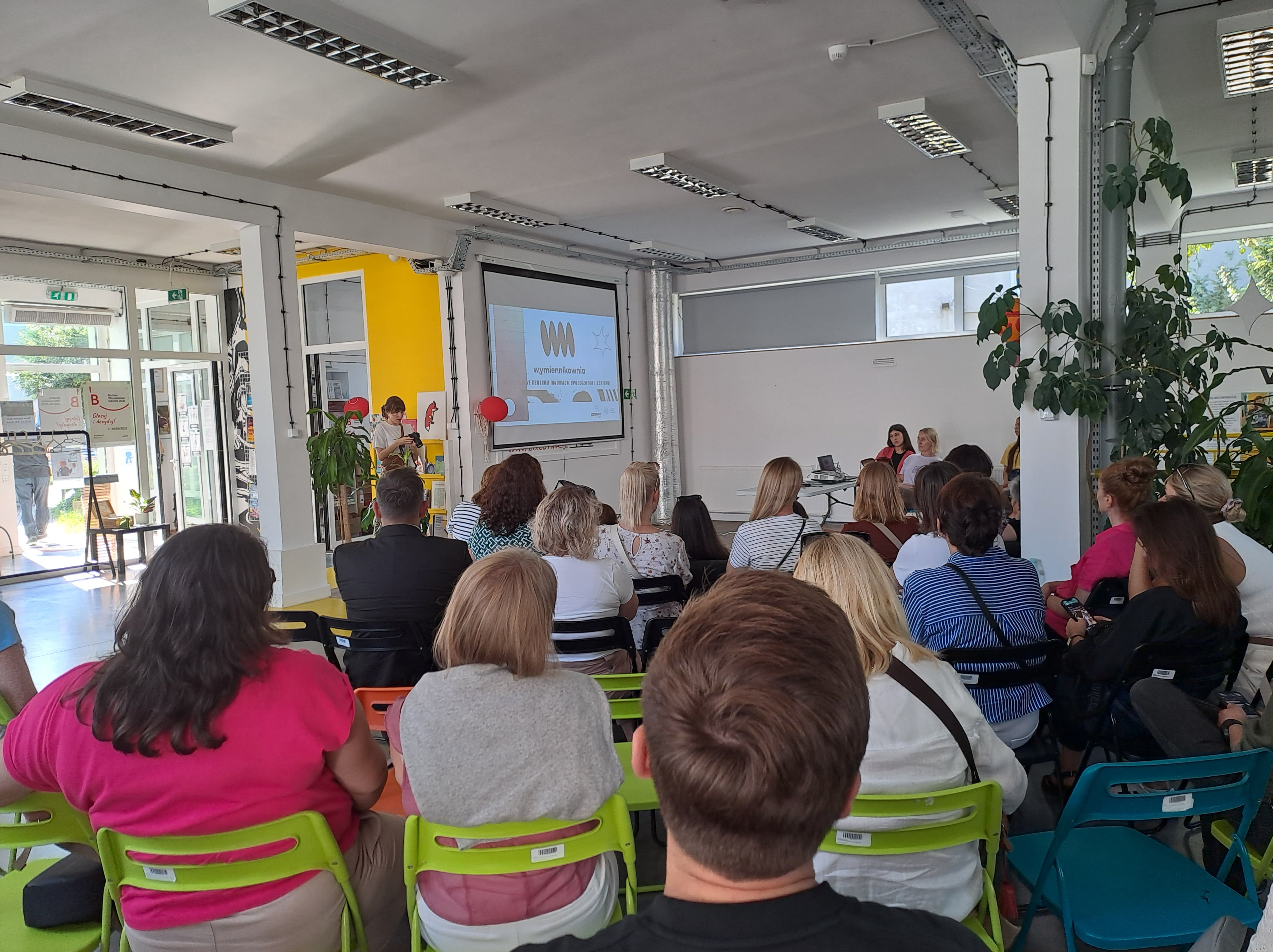 Grupa ludzi siedząca na krzesełkach w sali oglądająca prezentację