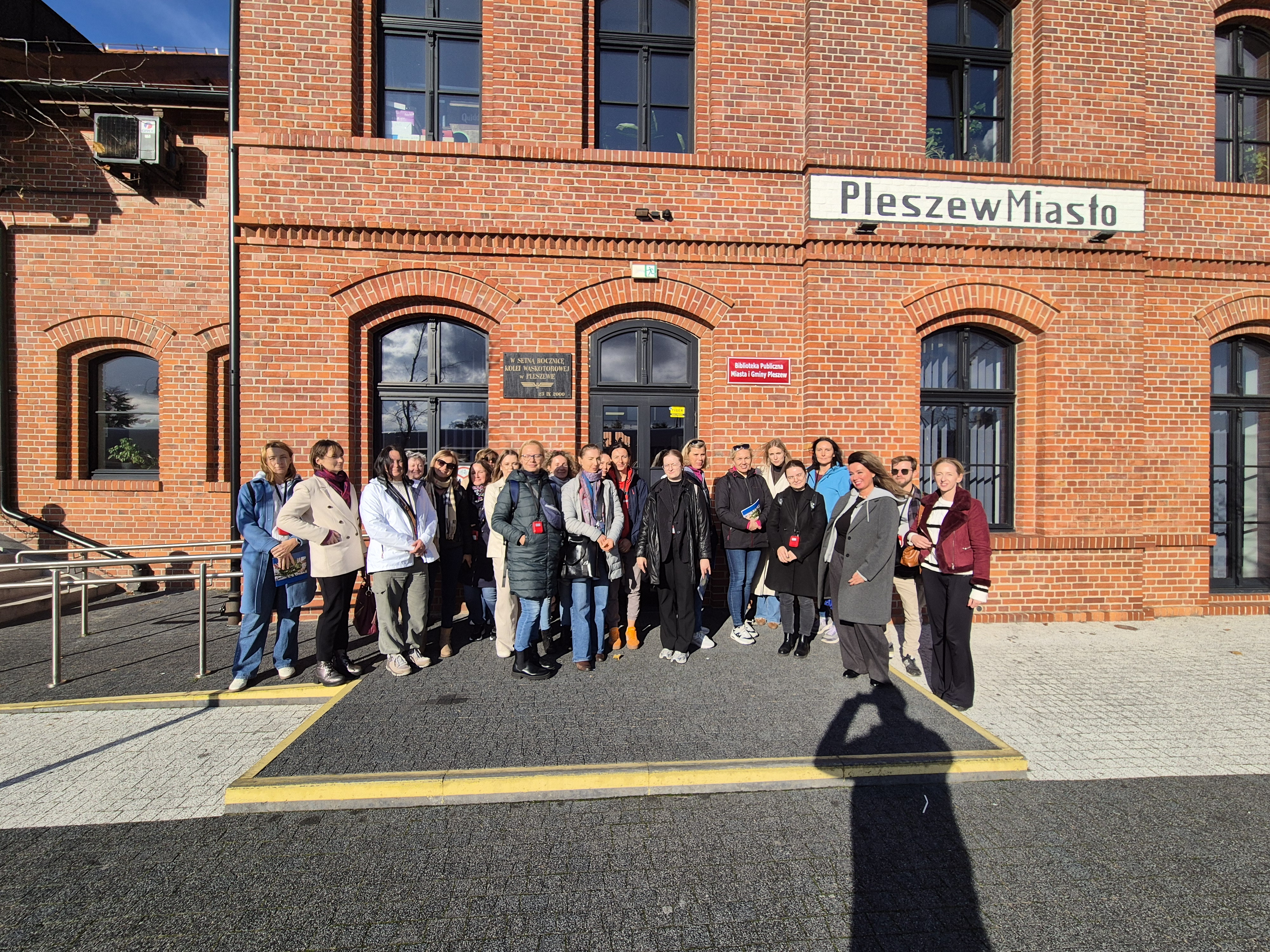 Grupa ludzi na tle dworca z elewacją z czerwonej cegły