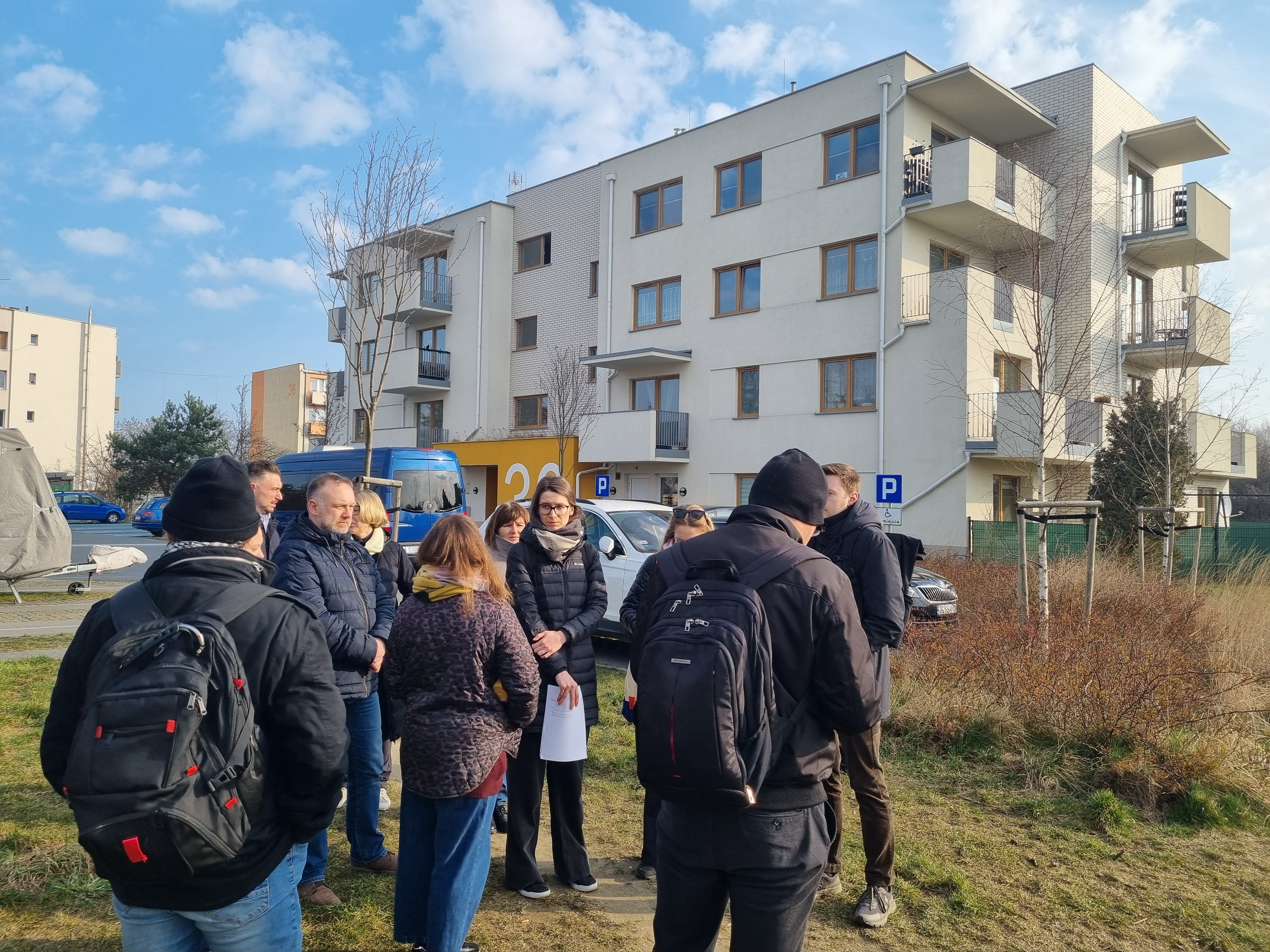 Grupa ludzi stojąca pod budynkiem mieszkalnym wielorodzinnym