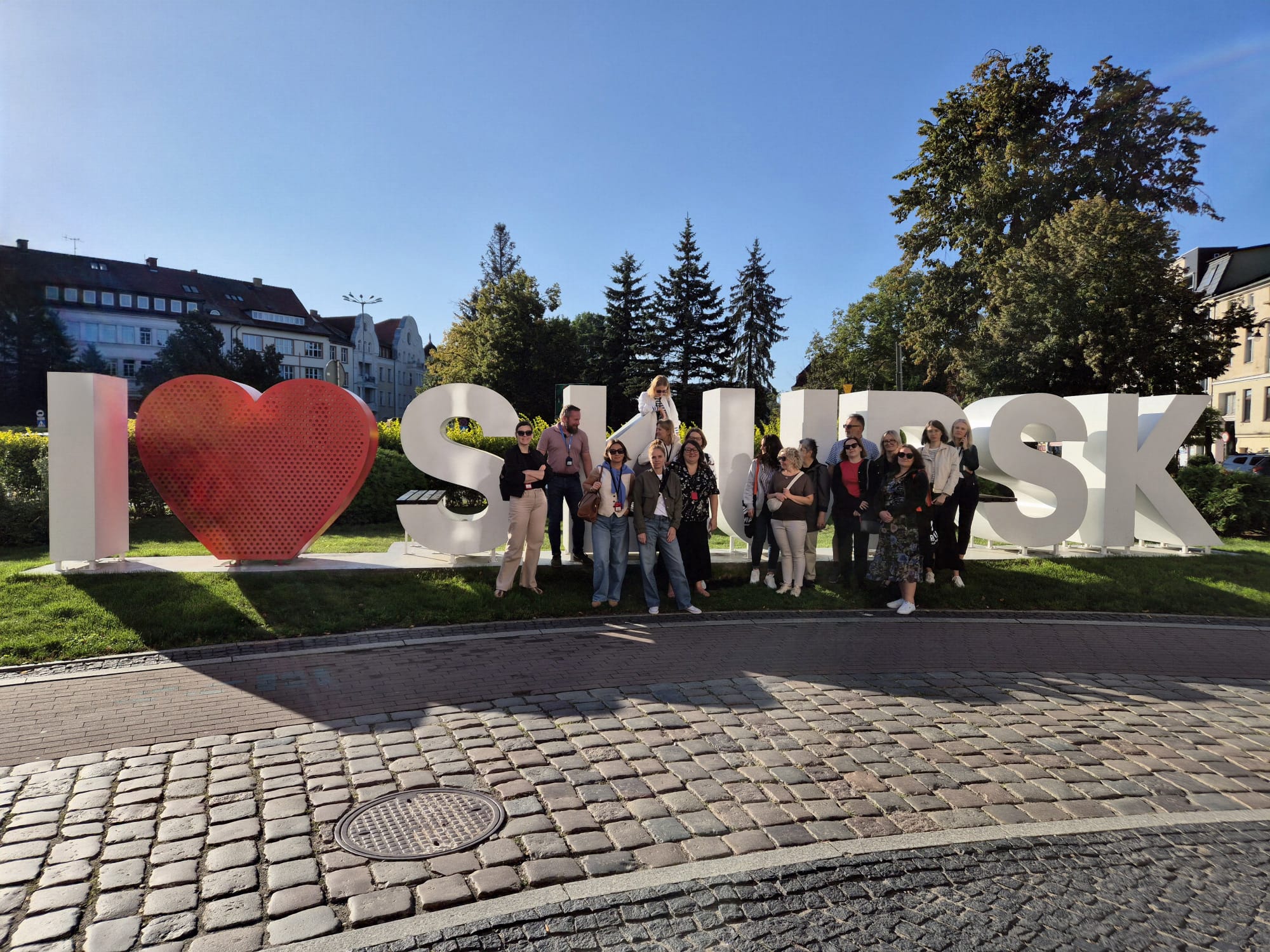 Grupa ludzi stojąca na tle dużego napisu "I love Słupsk"