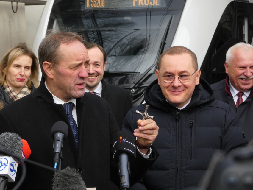 Grupa ludzi, wśród których jest marszałek Mieczysław Struk. Na pierwszym planie mikrofon, w tle pociąg