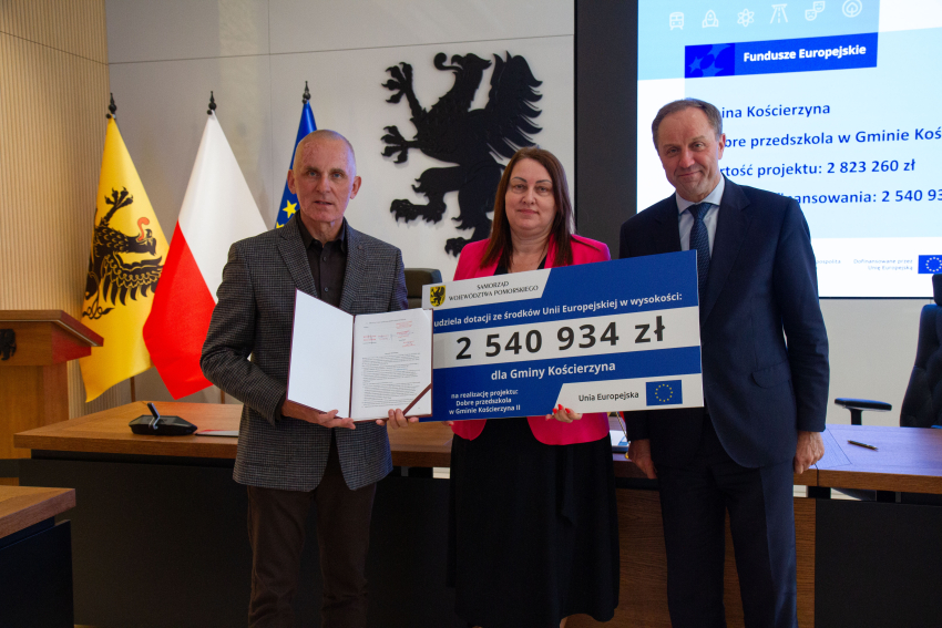 Marszałek Mieczysław Struk i przedstawiciele gminy trzymają czek informujący o dofinansowaniu