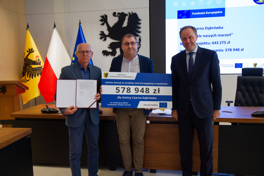 Marszałek Mieczysław Struk i przedstawiciele gminy trzymają czek informujący o dofinansowaniu