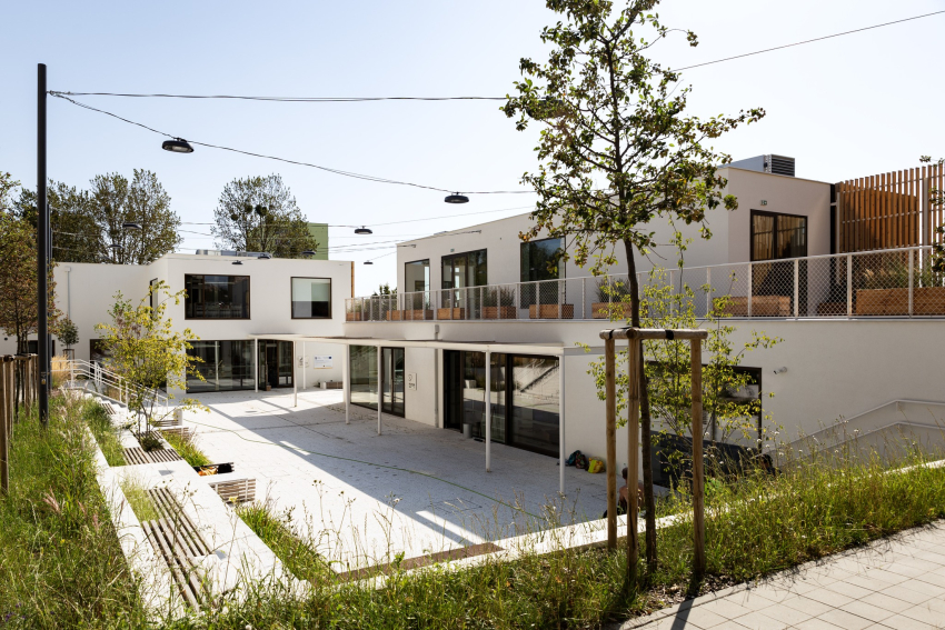 Dwa nowoczesne budynki, bryły są geometryczne o prostokątnych kształtach. W ich towarzystwie znajduje się też kilka drzew i trawnik