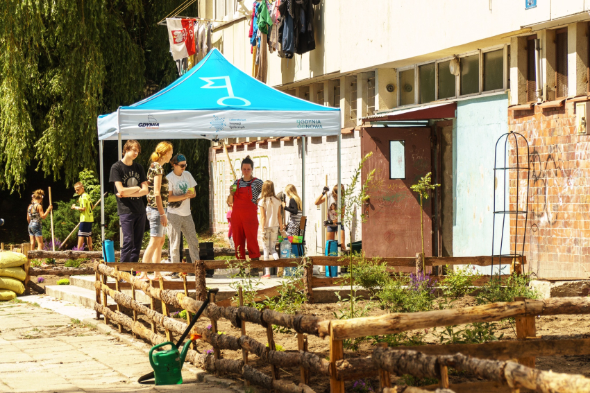 Dziewięć osób stoi i rozmawia w trakcie jakichś prac ogrodowych