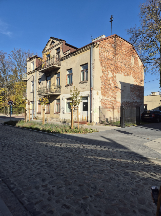 Kamienica ze zniszczoną elewacją stojąca przy wyremontowanej, wybrukowanej drodze