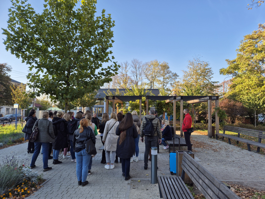 Grupa ludzi słuchająca przewodnika na małym placu pośród drzew