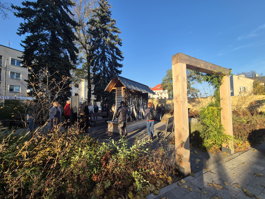 Ludzie na placu za drewnianą bramą stojący wokół drewnianej budki