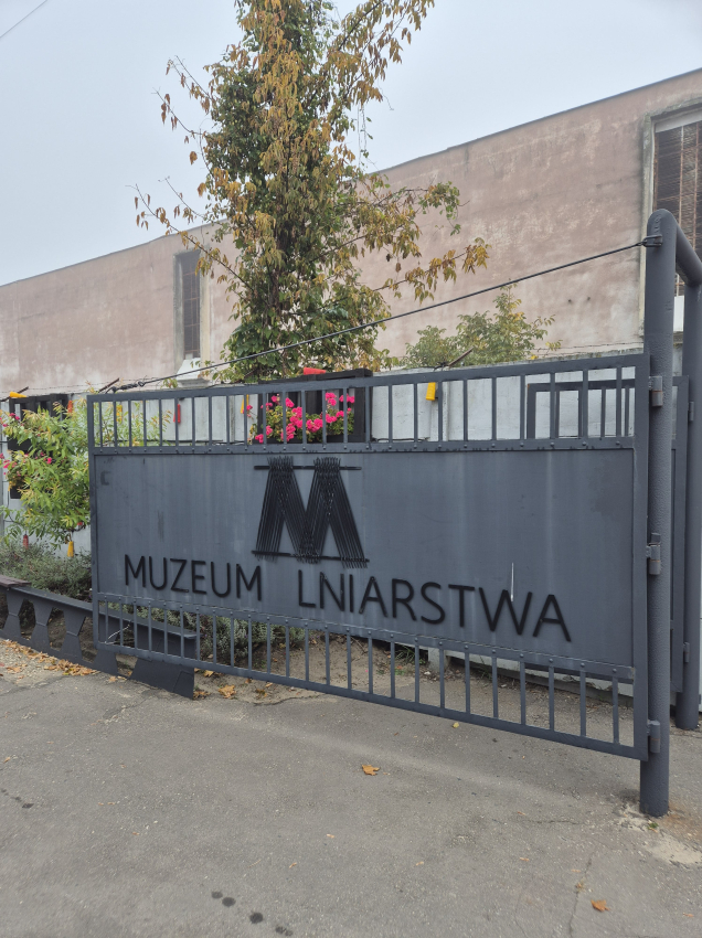 Metalowa brama z dużą literą M i napisem &quot;Muzeum Lniarstwa&quot;