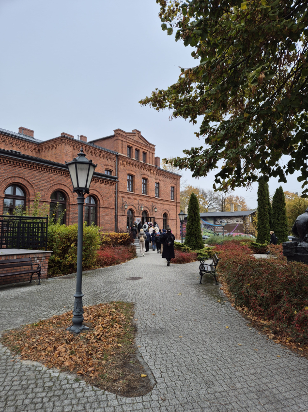 Grupa ludzi wchodząca do budynku z czerwonej cegły znajdującego się przy parku