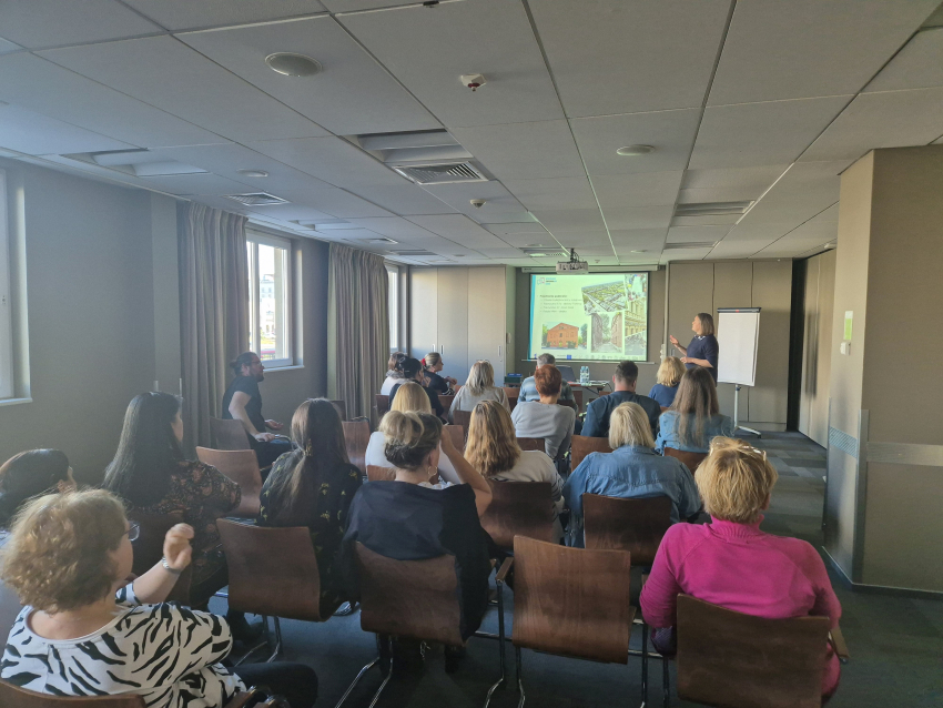 Sala wykładowa wypełniona ludźmi siedzącymi na krzesłach, zwróconymi w kierunku pulpitu z prezentacją dotyczącą rewitalizacji