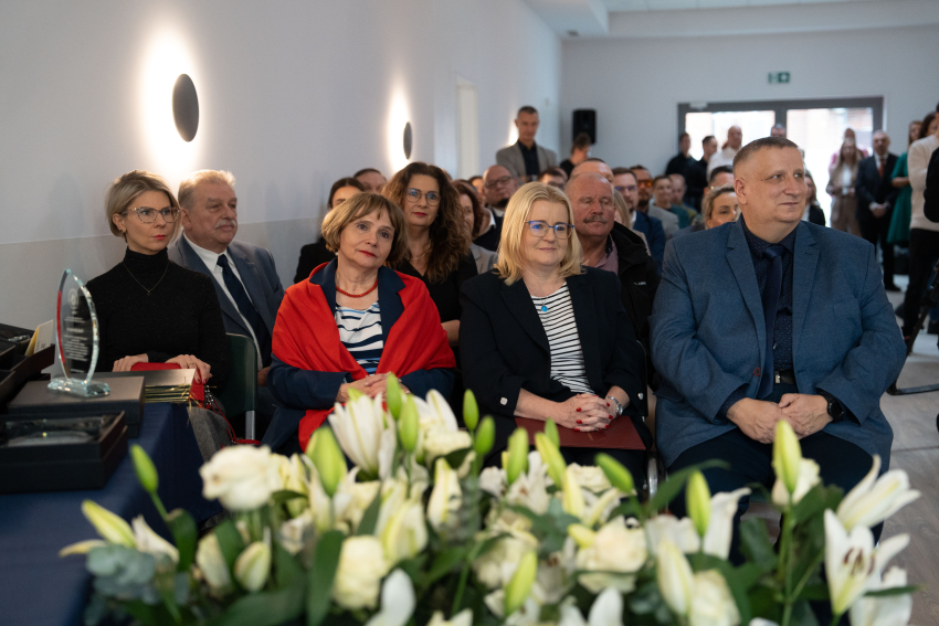 Grupa ludzi w sali siedzi na krzesłach