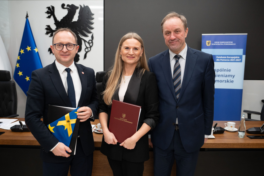 Marszałek Mieczysław Struk, wicemarszałek Marcin Skwierawski i jedna przedstawicielka władzy lokalnej prezentują podpisaną umowę i flagę Unii Europejskiej.
