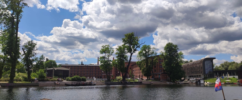 Wyremontowany budynek po starej fabryce. Przed nim woda i duże, stare drzewa