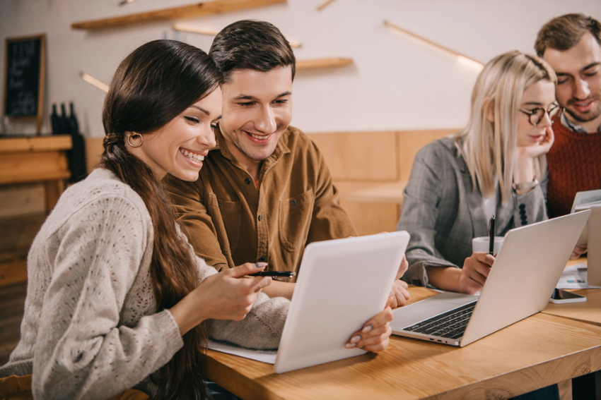 Dwie uśmiechnięte pary damsko-męskie siedzą przed dwoma laptopami.