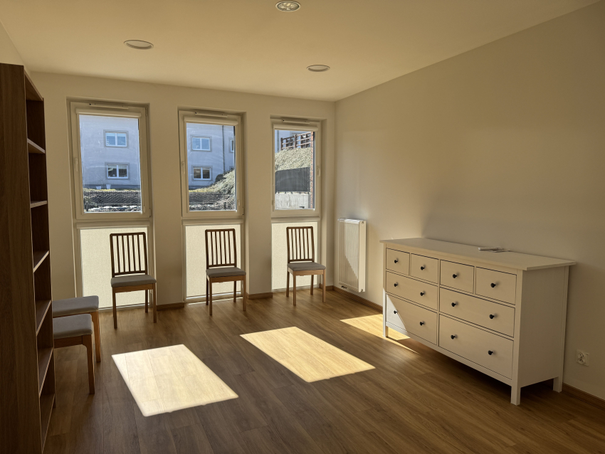 Pokój dla osoby z autyzmem w budynku. W ujęciu widać komodę, trzy krzesła oraz półka na książki