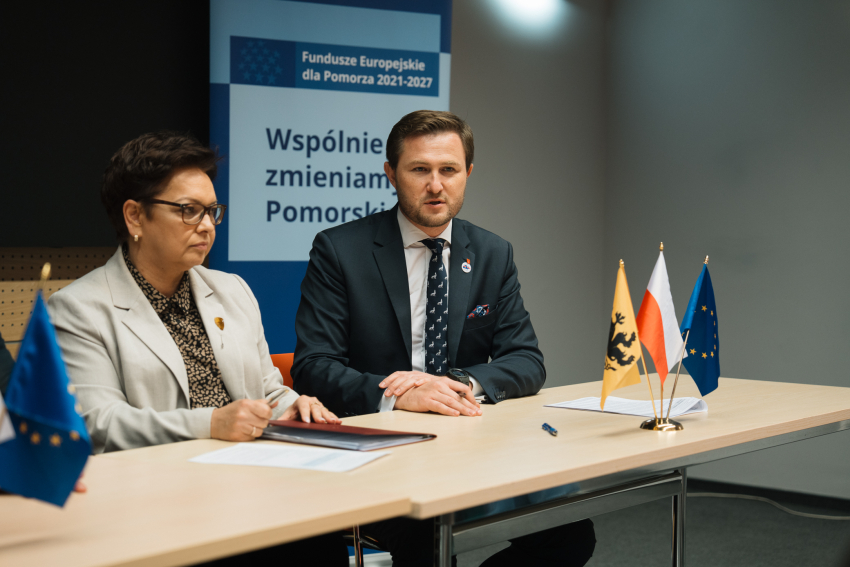 Zdjęcie przestawia dwie osoby siedzące przy stole prezydialnym.