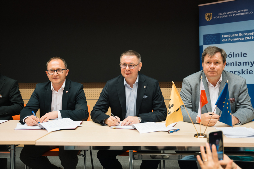 Zdjęcie przedstawia trzy osoby siedzące przy stole prezydialnym.