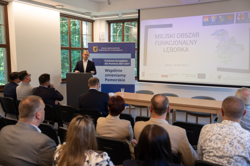 Ktoś stoi przy mównicy i przemawia do zebranych. W tle obraz rzutnika oraz rollup "Wspólnie zmieniamy Pomorskie"