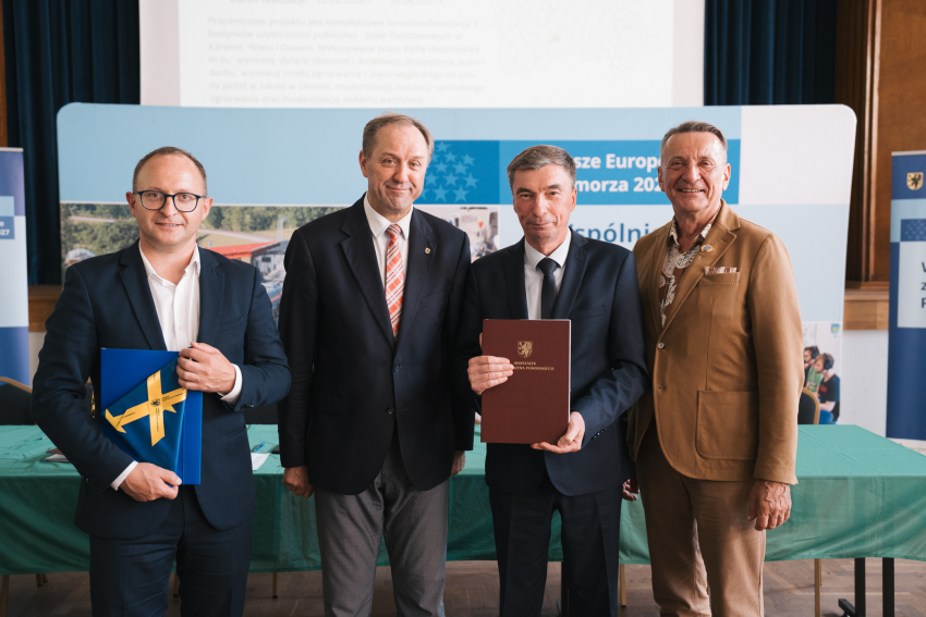 Marszałek Mieczysław Struk, wicemarszałek Marcin Skwierawski i wicemarszałek Leszek Bonna wraz z przedstawicielem jednej z gmin prezentują podpisaną umowę oraz flagę Unii Europejskiej.