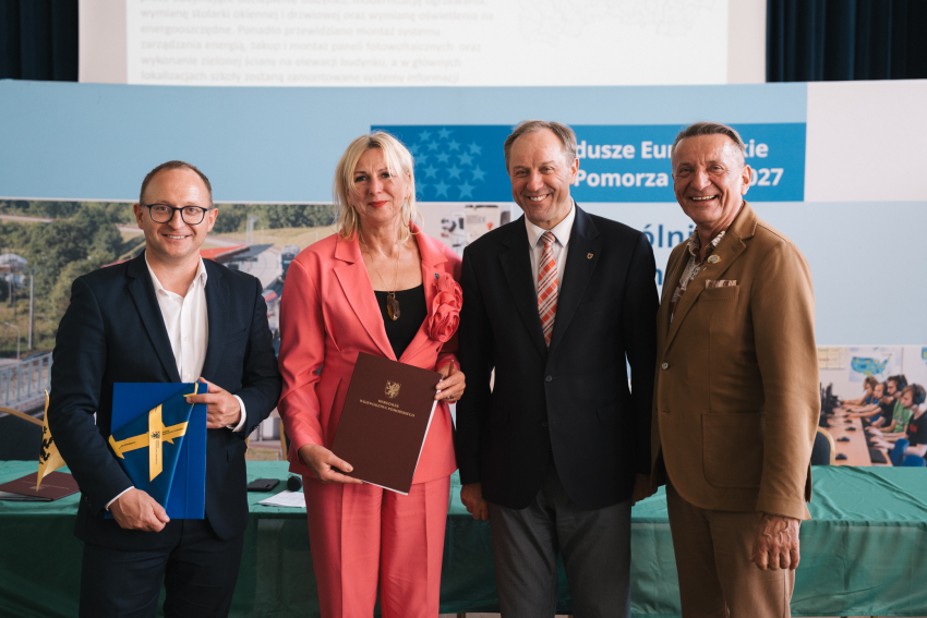 Marszałek Mieczysław Struk, wicemarszałek Marcin Skwierawski i wicemarszałek Leszek Bonna wraz z przedstawicielką jednej z gmin prezentują podpisaną umowę oraz flagę Unii Europejskiej.