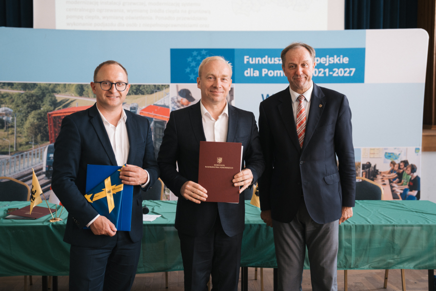 Marszałek Mieczysław Struk, wicemarszałek Marcin Skwierawski oraz przedstawiciel jednej z gmin prezentują podpisaną umowę oraz flagę Unii Europejskiej.