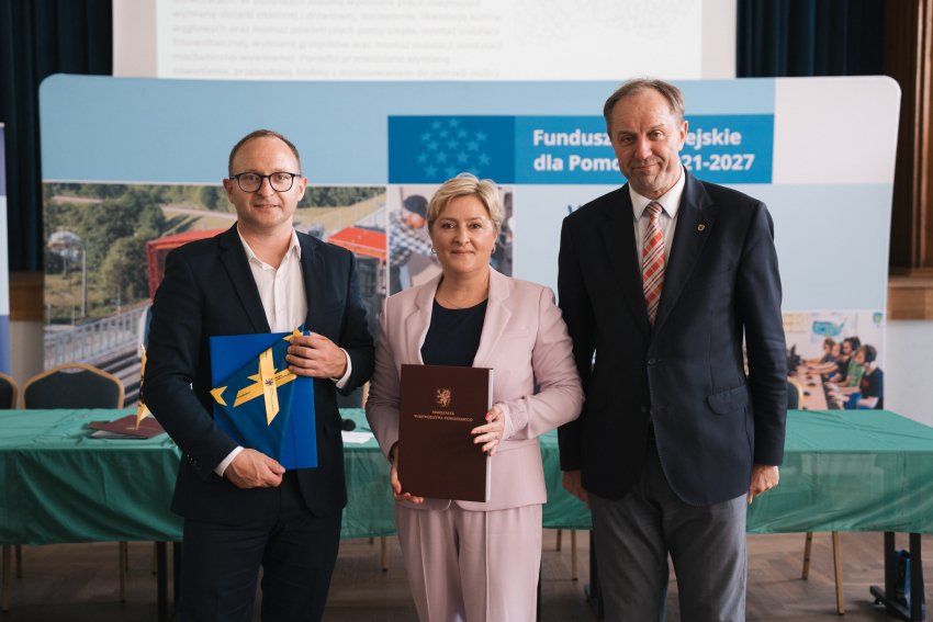 Marszałek Mieczysław Struk, wicemarszałek Marcin Skwierawski oraz przedstawicielka jednej z gmin prezentują podpisaną umowę oraz flagę Unii Europejskiej.