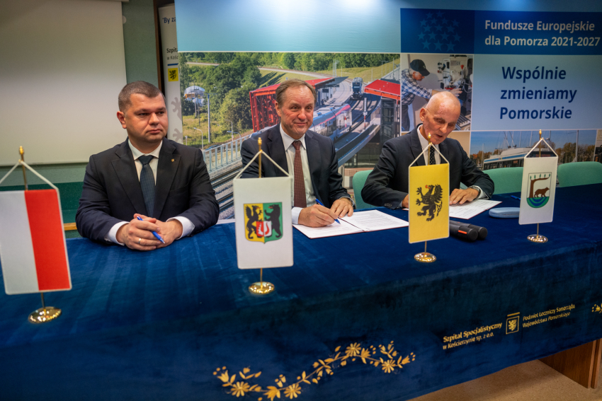 Marszałek Mieczysław Struk i dwie inne osoby siedzą przy stole prezydialnym i podpisują porozumienie