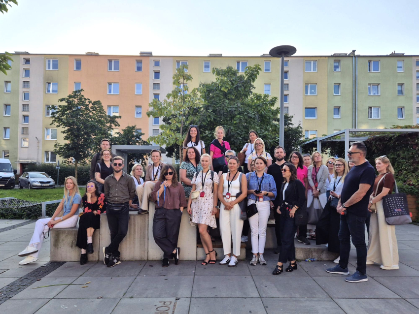 Grupa ludzi stojąca na placu przed blokiem mieszkalnym