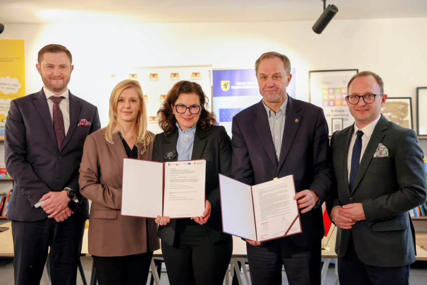 Pięć osób pozujących do zdjęcia w garniturach trzymając foldery z dokumentami