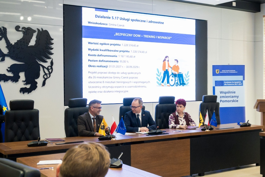 trzy osoby siedzą przy stole i podpisują umowy