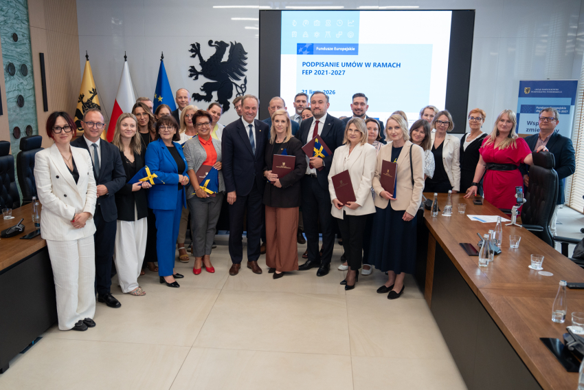 Grupa ludzi podczas uroczystego podpisania umów. 