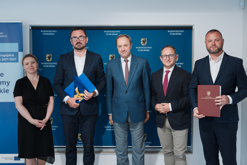 Marszałek Mieczysław Struk, wicemarszałek Marcin Skwierawski, wójt gminy Miłoradz Arkadiusz Skorek oraz dwie inne osoby pozują do uroczystego zdjęcia prezentując podpisaną umowę oraz flagę UE