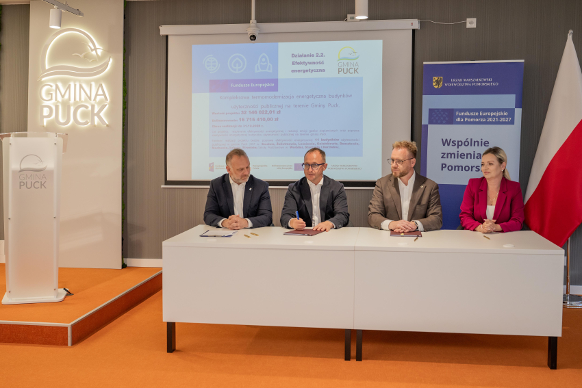 wicemarszałek Marcin Skwierawski oraz trzy inne osoby siedzą przy stole prezydialnym i podpisują umowę o dofinansowanie