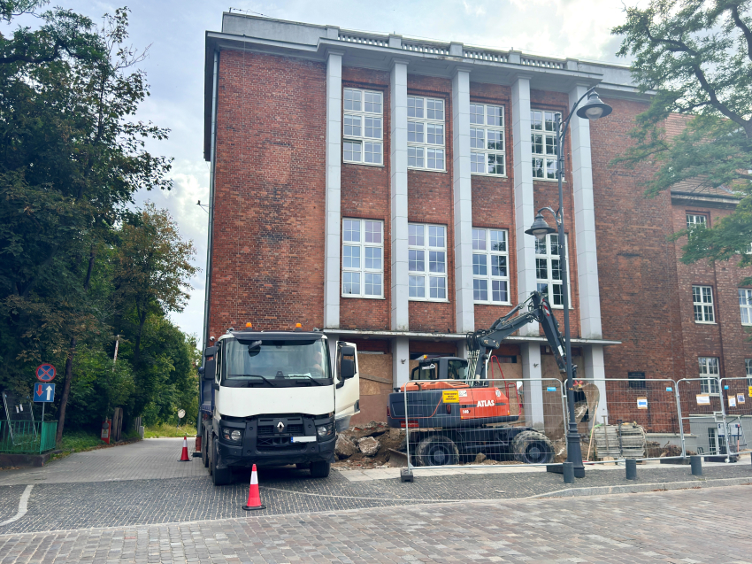 Budynek przy ul. Augustyńskiego 1 a przed nim koparka i ciężarówka. Prowadzone są prace budowlane.
