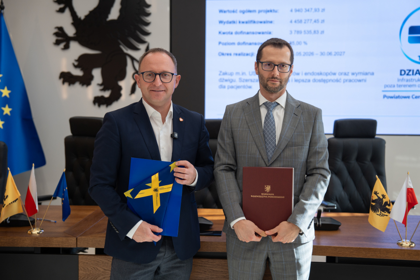 Wicemarszałek Marcin Skwierawski oraz przedstawiciel Powiatowego Centrum Zdrowia Sp. z o.o. pozują do uroczystego zdjęcia prezentując podpisaną umowę o dofinansowanie oraz flagę UE