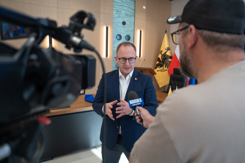 Wicemarszałek Marcin Skwierawski udziela wywiadu dla telewizji. Na pierwszym planie kamera oraz dziennikarz, na drugim widoczny wicemarszałek
