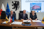 Marszałek Mieczysław Struk, wicemarszałek Marcin Skwierawski oraz przedstawicielka władz regionu siedzą przy stole prezydialnym i podpisują umowę