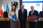 marszałek i dwie inne osoby pozują do zdjęcia eksponując podpisaną umowę oraz flagę UE