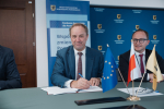 Marszałek Mieczysław Struk oraz wicemarszałek Marcin Skwierawski siedzą przy stole prezydialnym i podpisują umowę o dofinansowanie