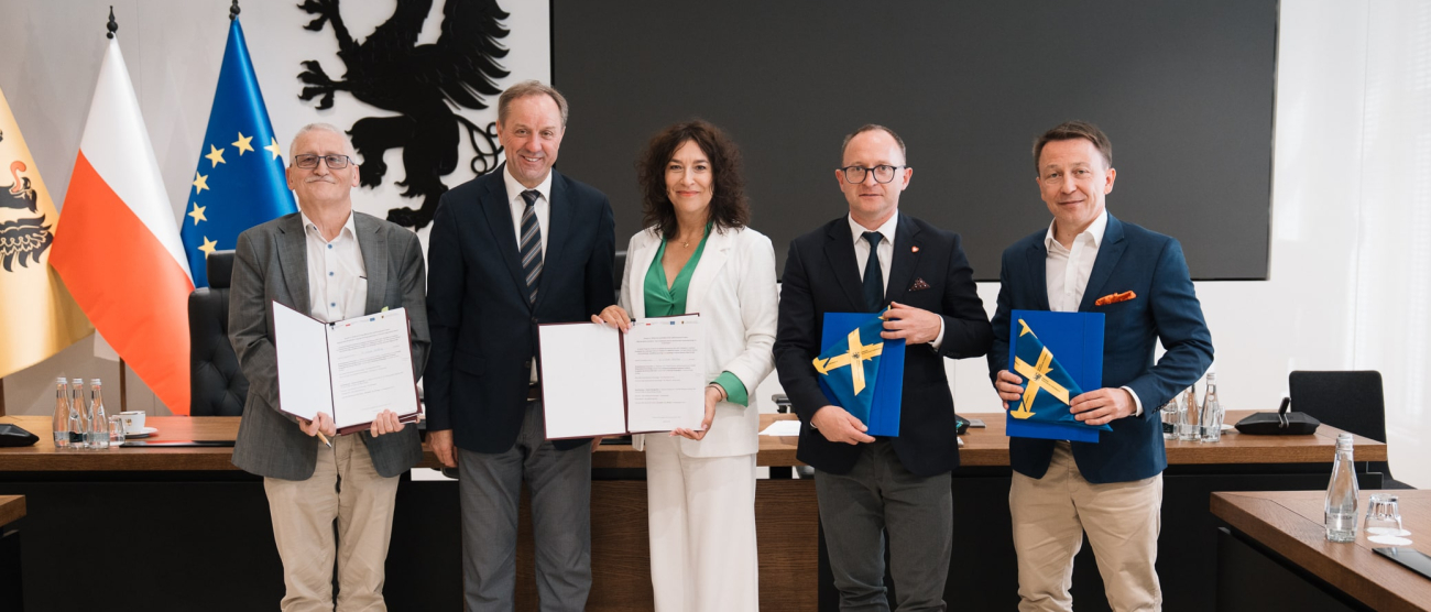 Marszałek Województwa Pomorskiego oraz wicemarszałek Marcin Skwierawski wraz z trzema innymi osobami prezentują podpisane umowy oraz flagi Unii Europejskiej