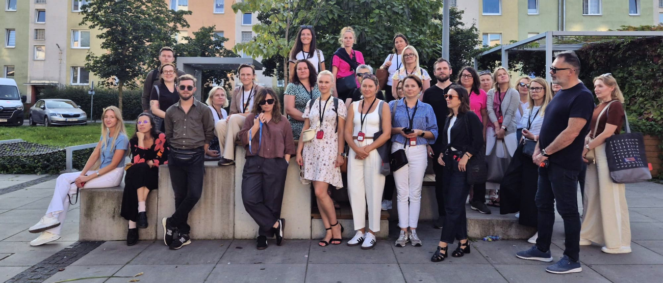 Grupa ludzi stojąca na placu przed blokiem mieszkalnym