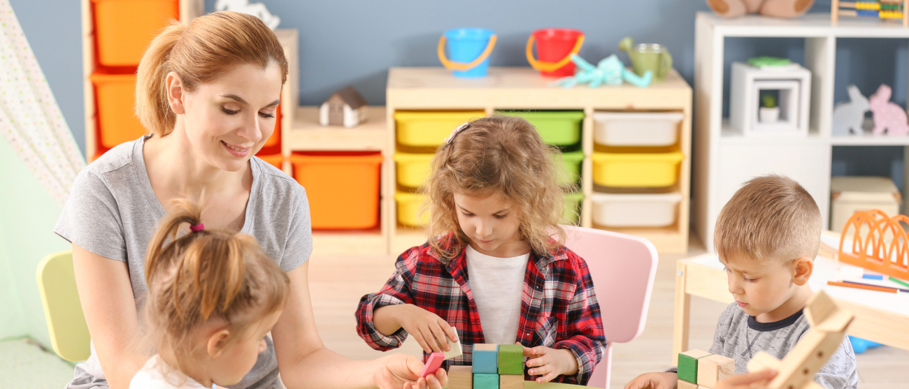 Przedszkolanka i czworo dzieci przy stoliku bawi się klockami 