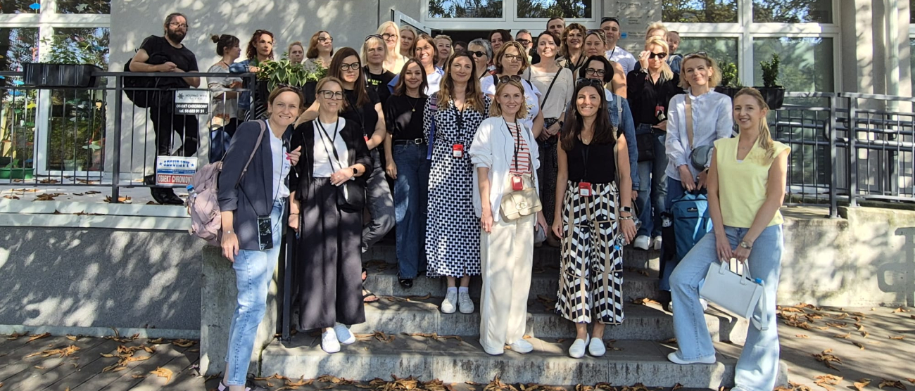 Grupa ludzi stojąca na schodach przy wejściu do budynku