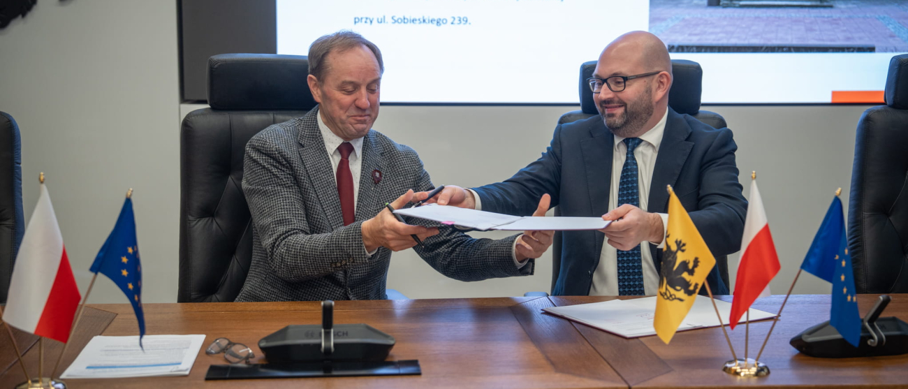 Dwie osoby przekazują sobie umowę do podpisu 