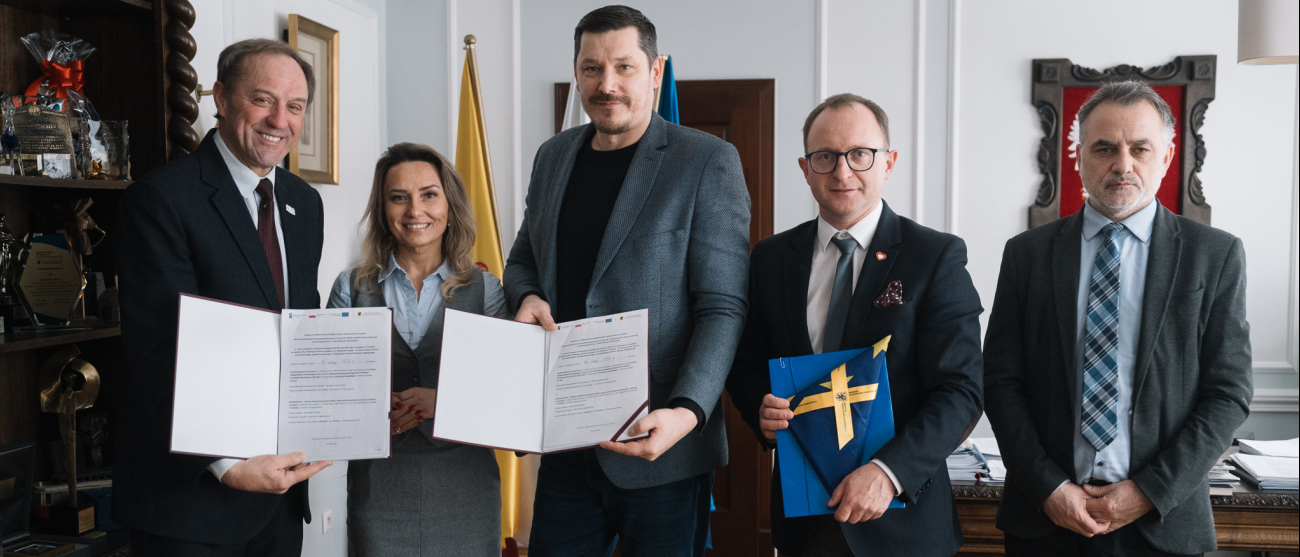 Od lewej: marszałek województwa pomorskiego Mieczysław Struk, przedstawicielka Miejskiego Zakładu Komunikacji w Słupsk oraz prezes tego zakładu, wicemarszałek Marcin Skwierawski oraz dyrektor Departamentu Programów Regionalnych Jan Szymański. Zebrane osoby pozują do uroczystego zdjęcia prezentując podpisane umowy oraz flagę Unii Europejskiej