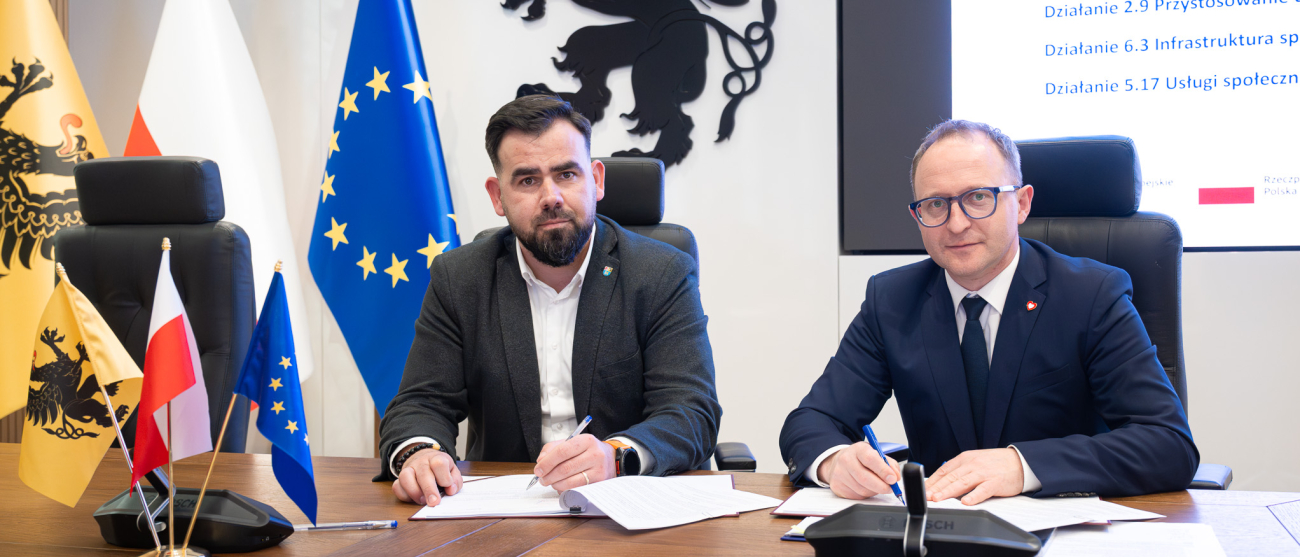 Dwie osoby siedzą za stołem i podpisują umowę. Po lewej Starosta Powiatu Lęborskiego - Pan Tomasz Litwin, po prawej - wicemarszałek województwa pomorskiego - Marcin K. Skwierawski. 