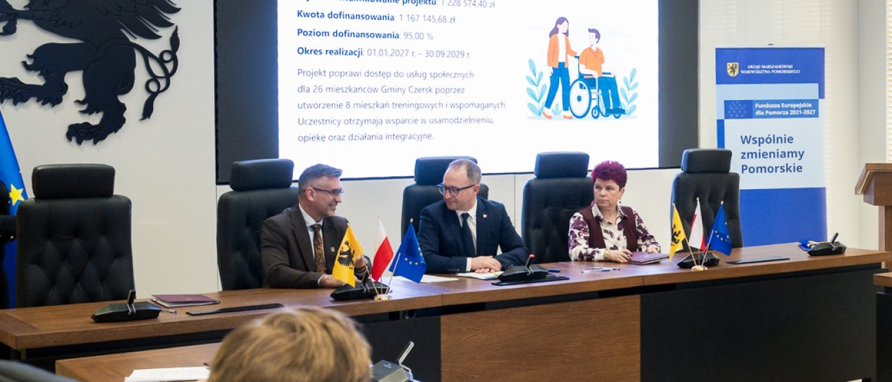 trzy osoby siedzą przy stole i podpisują umowy