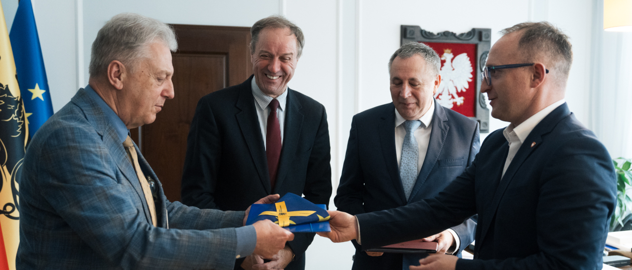 Dwóch wiceprezesów Copernicus Podmiot Leczniczy Sp. z o.o. oraz marszałek Mieczysław Struk i wicemarszałek Marcin Skwierawski pozują do zdjęcia i przekazują złożoną flagę UE gościom