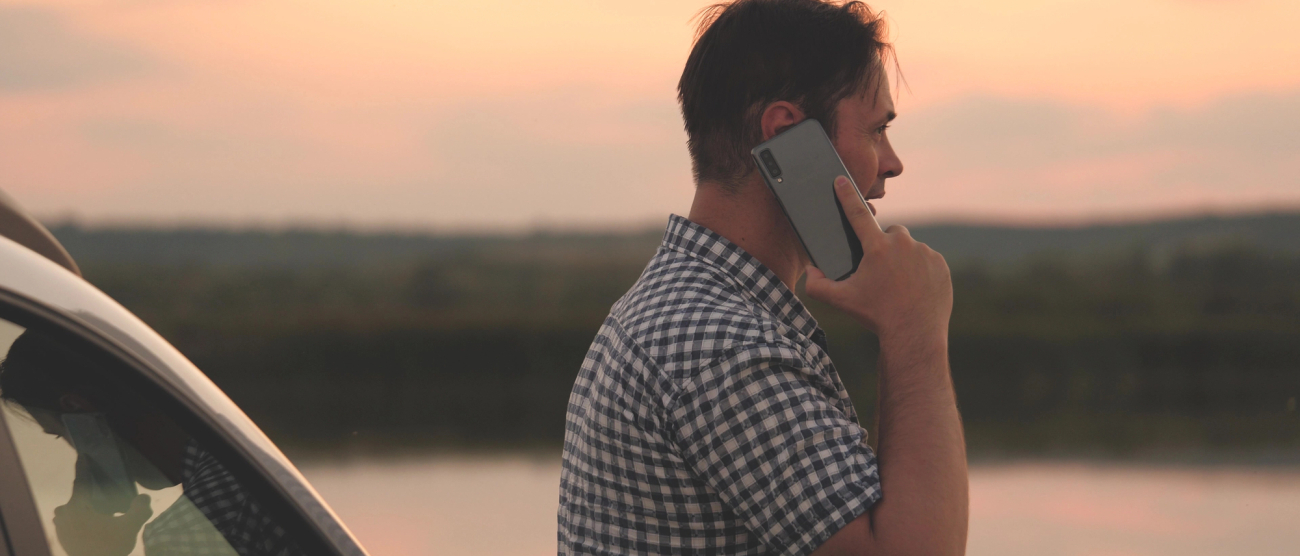 Mężczyzna z telefonem w ręku. W tle samochód